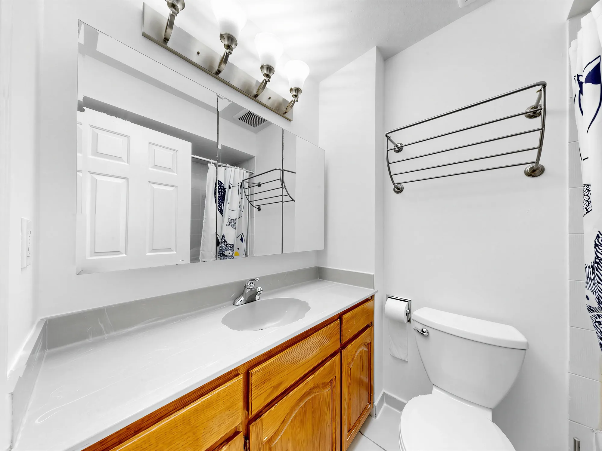 A bathroom with a long vanity, a wide mirror and a lit bar above it