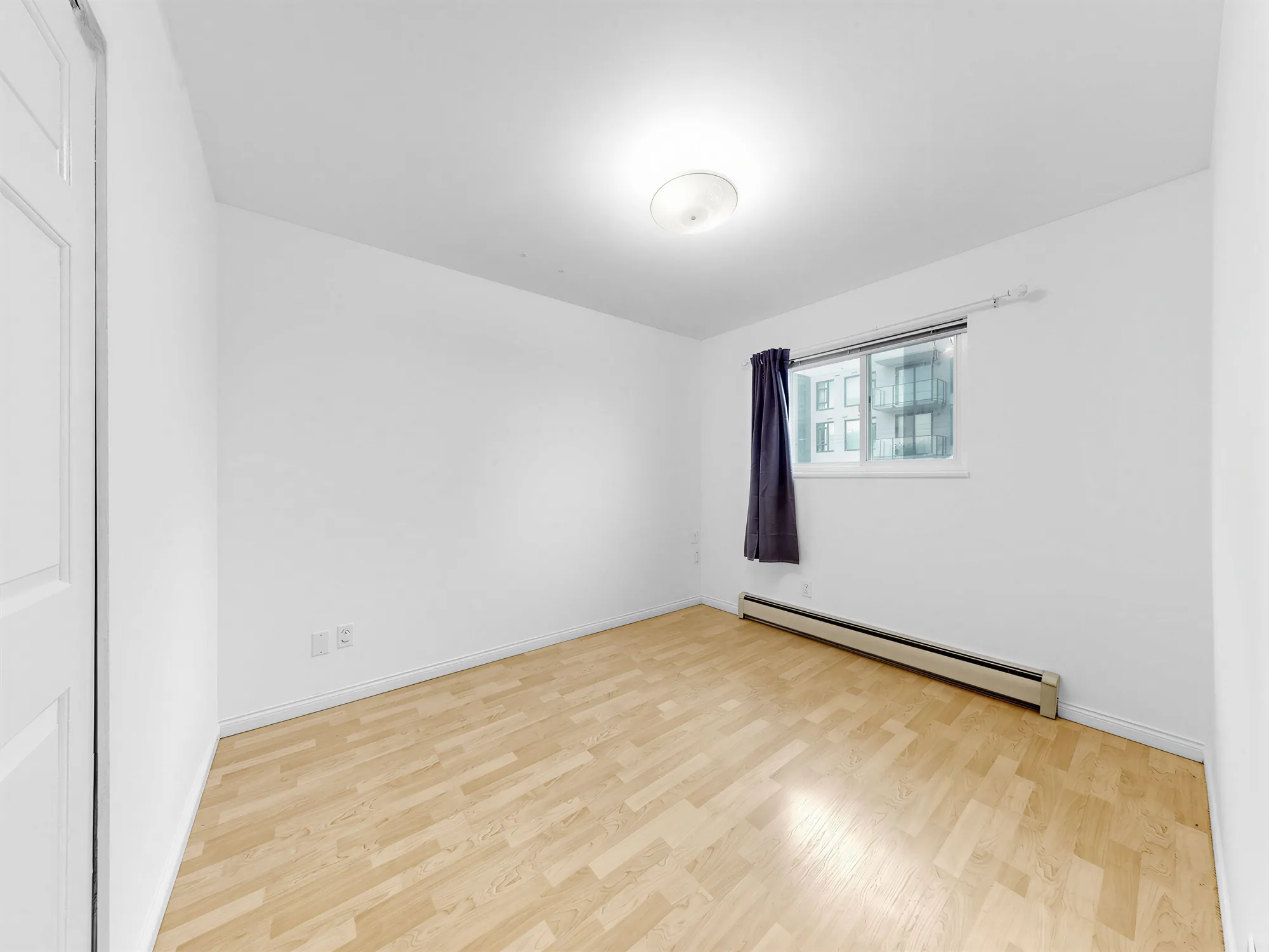 A bedroom with a window on the right and a plain flush ceiling light