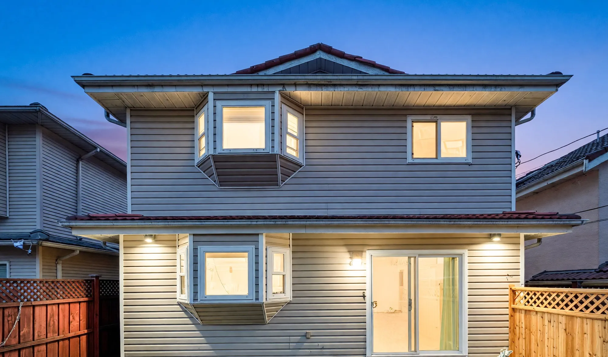 8377 Shaughnessy Street seen from the garden at dusk, the windows lit