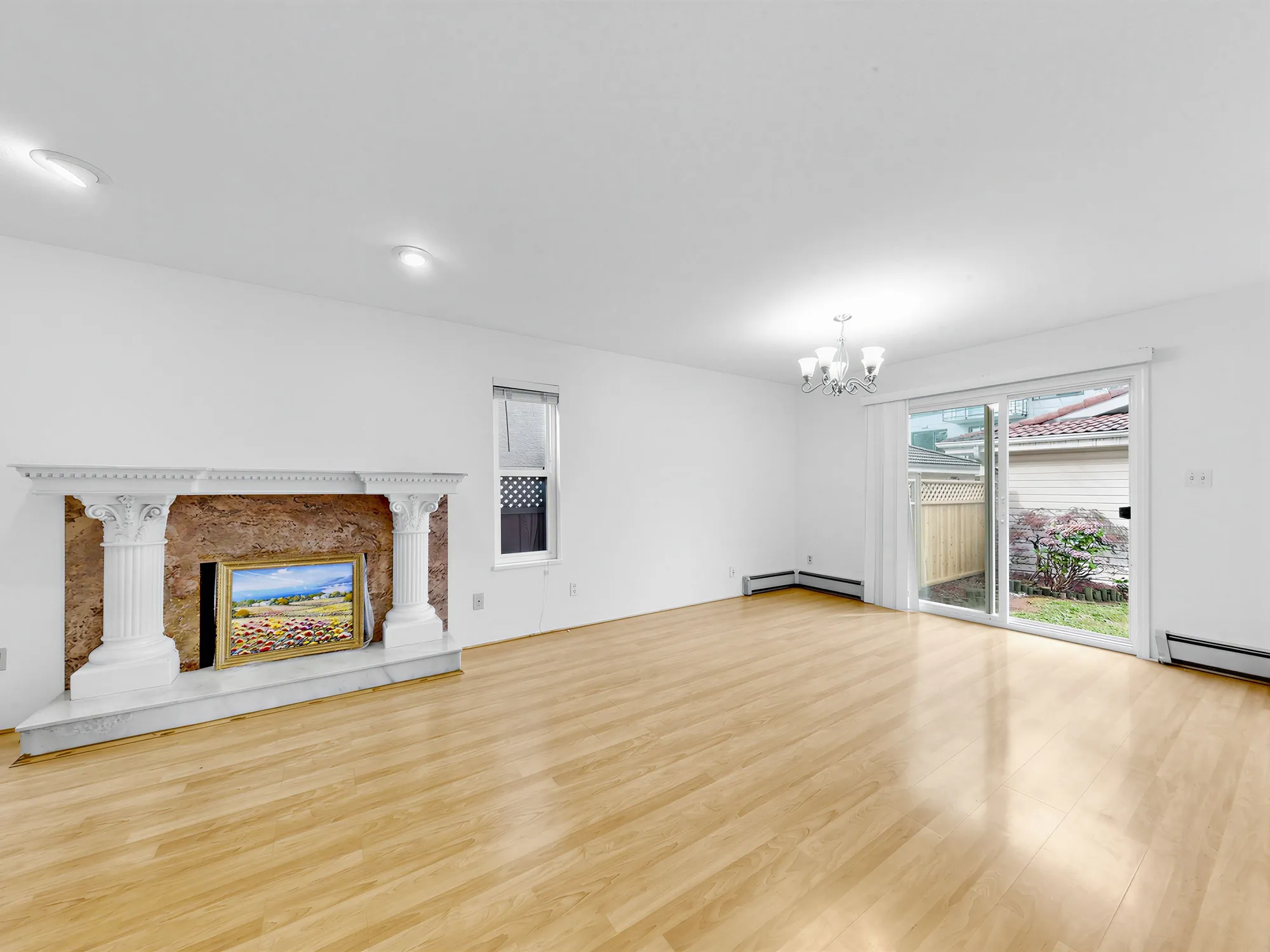 The living room, empty, with a painted mantel on the left and a sliding door to the garden